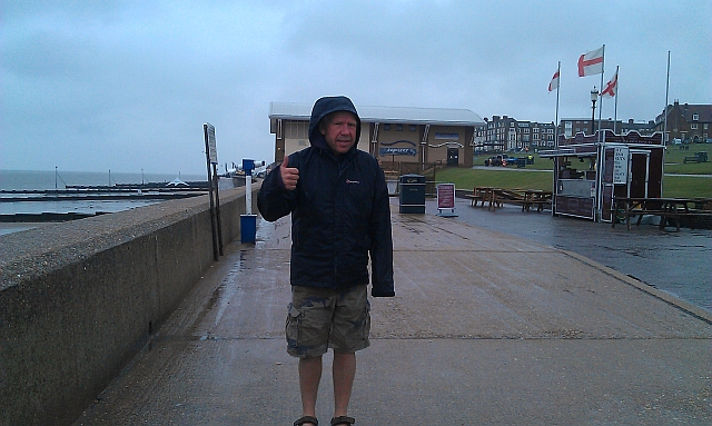 iw in a rain jacket and shorts on a concrete sea defence in the wind and rain at hunstanton